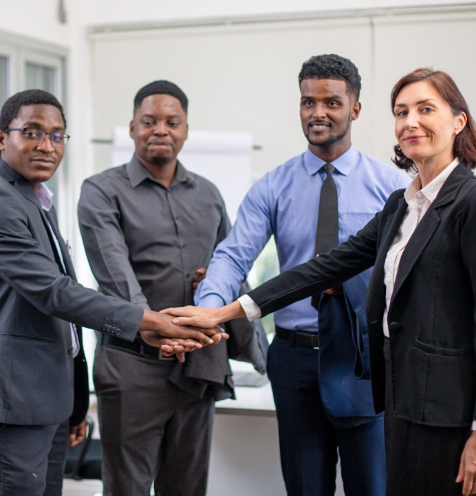 United coworkers standing with their hands together in modern office, celebrating victory, teambuilding and unity